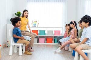 Asian beautiful young woman teacher teaching mixed race kids at school. Attractive Instructor master female explain and educate reading book with child student kindergarten pre school in classroom.