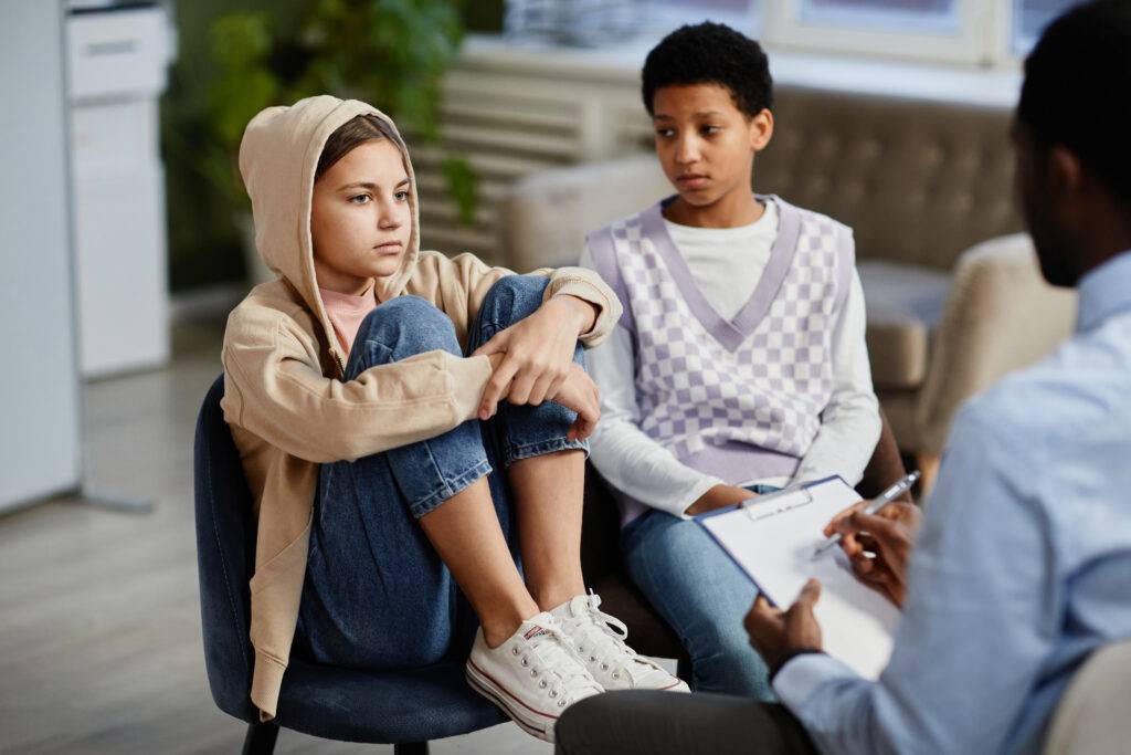 Portrait of teenage girl wearing hoodie in group therapy session with diverse children